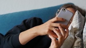  Eine junge Frau liegt auf einem Sofa und schaut auf ihr Smartphone. | picture alliance/dpa