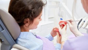 Eine Patientin und eine medizinische Fachkraft schauen gemeinsam auf ein Gebiss mit Zahnspange. | picture alliance / Zoonar